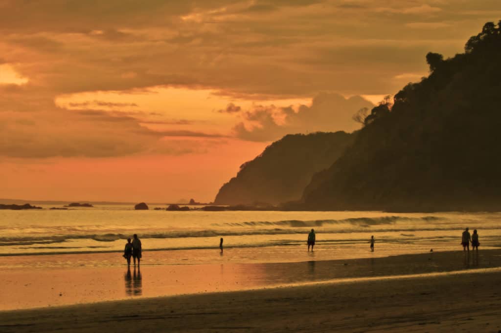 A group of people walking on the beach in Costa Rica at sunset.