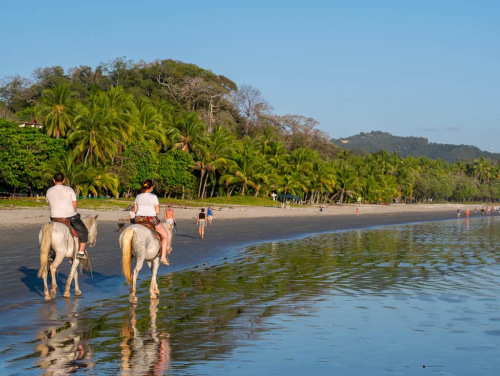 Two people riding horses on a Costa Rican beach.