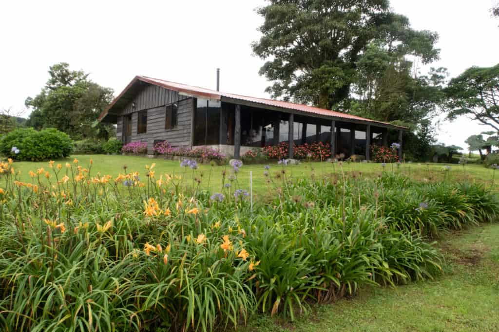A cabin surrounded by a colorful array of flowers in the middle of a grassy field in Costa Rica.